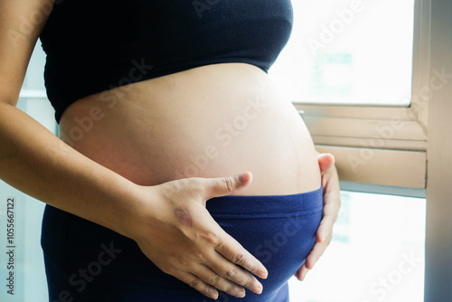 Pregnant asian women standing with window light shw belly