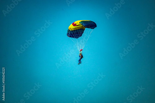 A parachutist flies on a blue and yellow parachute in a clear blue sky