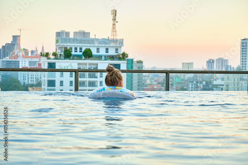 A beautiful little girl swims in a pool with an inflatable circle on the roof of a skyscraper in Phnom Penh, Cambodia.