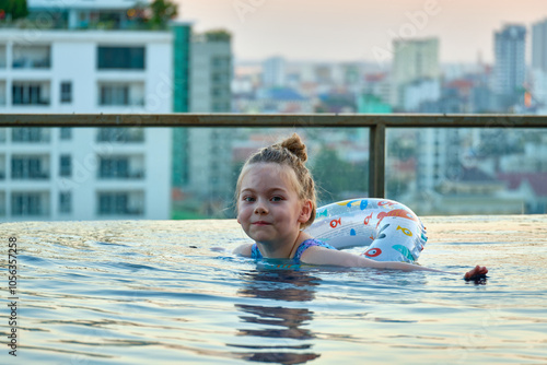 A beautiful little girl swims in a pool with an inflatable circle on the roof of a skyscraper in Phnom Penh, Cambodia.