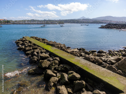 Detailed plan of a stone jetty in the middle of the sea surrounded by stone cubes with berdin in Hondarribia and Hendaye in the background.