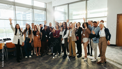 Diverse group at seminar happily waving inside modern conference room with large windows and bright natural light