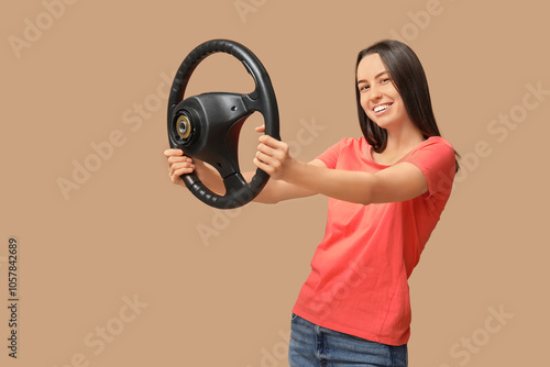 Beautiful young woman with steering wheel on beige background