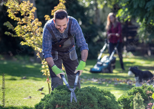 Man and woman taking care of garden in autumn time, trimming bushes and mowing lawn