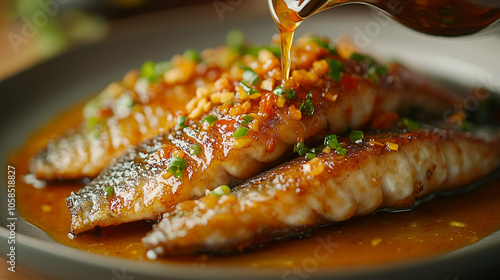 Succulent grilled fish fillets drizzled with a rich, savory garlic and herb sauce. The fish is garnished with fresh green onions and chili, adding vibrant color and flavor.