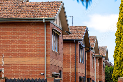 A row of traditional brick townhouses with repetitive architectural design and uniform terracotta roofing in a suburban residential neighborhood of Australia. Exterior of multi-family housing units. 