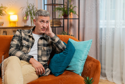 Thoughtful young man guy male sitting at home looks pensive thinks over life concerns or unrequited love, suffers from unfair situation. Problem, break up, depressed feeling bad annoyed, burnout.