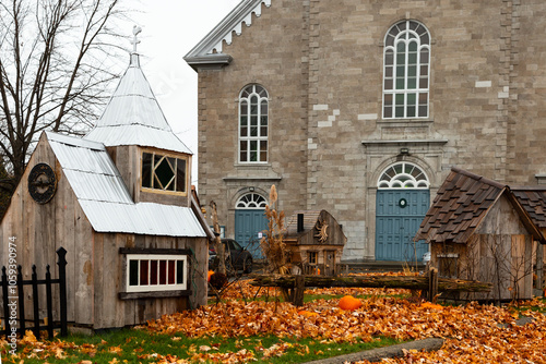 Cute seasonal decorations including a miniature church and other wooden buildings in front of the historic 1858 Saint-Michel stone church, Saint-Michel-de-Bellechasse, Quebec, Canada