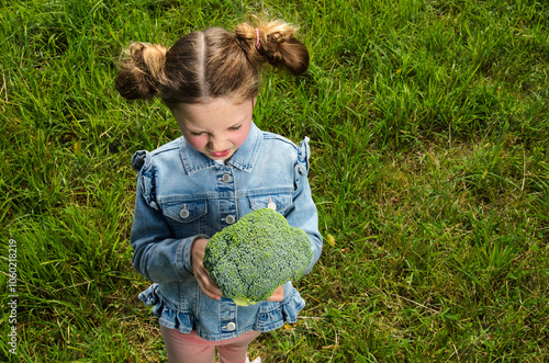 Girl of six years old holds a brocolli in her hand.