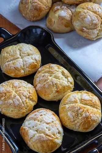 Buns, newly prepared Swiss sweets in the oven and with sugar glaze at the top on black tray with gold edge, and next to its side Swiss sweet buns on baking paper