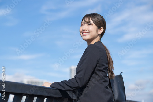 青空背景でスーツを着た笑顔の若い女性 就職や新卒採用のビジネスイメージ 未来や希望を見つめる