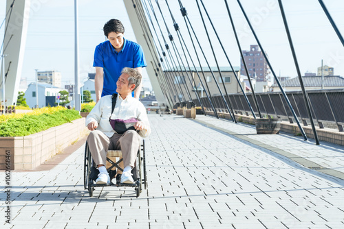 介護、介護士、車椅子、外出、ヘルパー、シニア、高齢者、お年寄り、街、笑顔、都市、社会、ウェルネス、福祉、ケアスタッフ、スタッフ、介助、老後、介護福祉士、橋、道路、歩道、バリアフリー、障害者、障害、ホームヘルパー、散歩、屋外、サービス、サポート、訪問、介護員、自立支援、リハビリ、健康、ヘルスケア、老人ホーム、付き添い、施設、青空、ポジティブ、元気、明るい、リラックス、男性、デイサービス、日本人、歩く