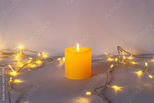 Home interior, soft light from a burning candle and a yellow garland, on a colored background of neutral colors.