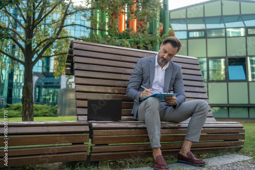 Businessman hand working with new modern computer and writing. accounting concept. Businessman working using calculator with money stack in park. Attractive smiling businessman working