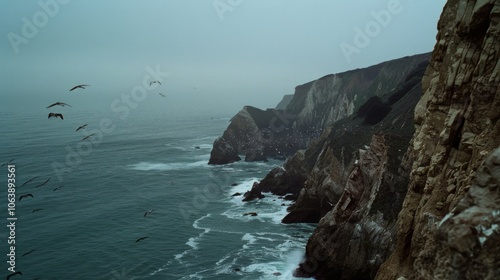 An overcast sky looms over the rugged cliffs as a flock of birds dances above the wild, restless sea, capturing nature's fierce dynamism.