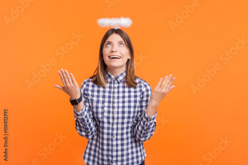 Surprised smiling woman with brown hair and nimb over head standing with raised arms looking up