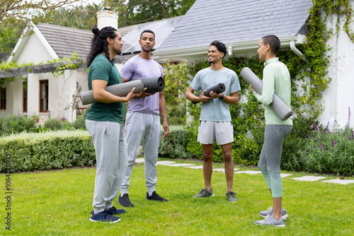 Young multiracial friends holding yoga mats, chatting and smiling in garden