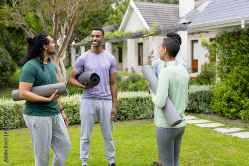 multiracial friends holding yoga mats chatting happily in garden before outdoor workout