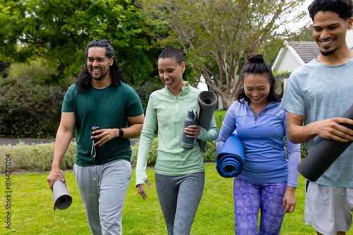 multiracial friends walking in park carrying yoga mats, smiling and enjoying outdoor exercise