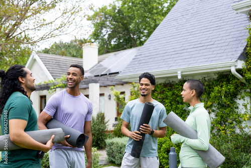 Young multiracial friends laughing and holding yoga mats outside house with solar panels