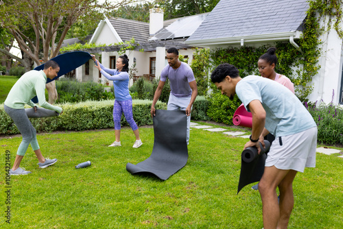 Young multiracial friends setting up yoga mats for outdoor exercise in garden