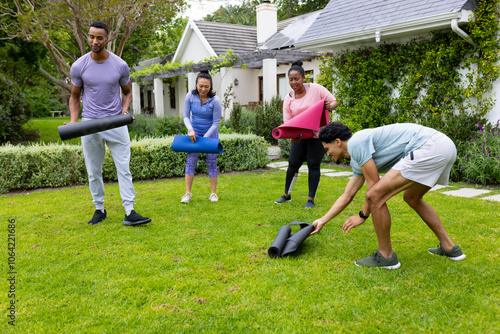 multiracial friends preparing yoga mats for outdoor exercise in garden, enjoying fresh air