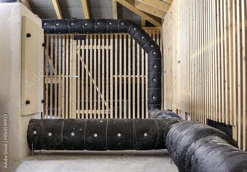 Exhaust duct or ventilation duct in attic of building. HVAC duct work installation. Large black insulated ductwork in attic with wooden storage units. Selective focus. Lucerne, Switzerland.