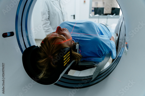 Mature female patient lying on table entering MRI machine in hospital setting. Medical professional in white coat standing nearby. Professionalism, precision, and modern health technology.