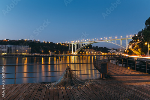 Fishing net laying on pier with illuminated Arrabida bridge at blue hour in afurada, Gaia, Porto, Portugal