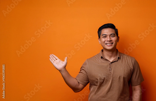 Asian Man Pointing at Empty Space in Front of Orange Background