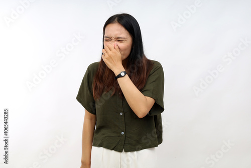 Young asian woman wearing casual shirt smelling something stinky and disgusting, intolerable smell, holding breath with fingers on nose. bad smell