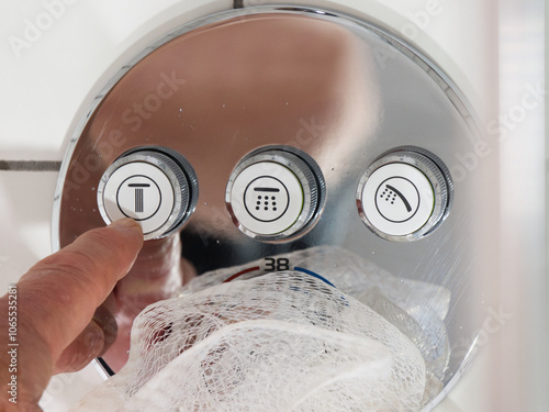 Closeup of a finger pressing the start or stop button option on a modern shower control panel to switch it on or off.