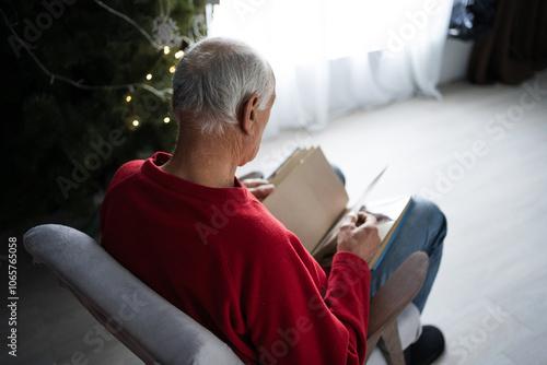 View from shoulders on widower holding photo-album looking photos and remembering deceased wife. Close-up