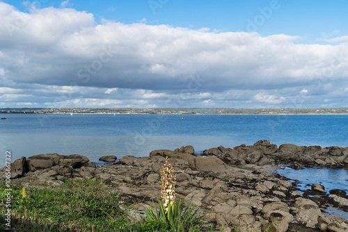 Vue sur les rochers de Beg Meil et l'océan Atlantique, sous un ciel bleu parsemé de nuages. L’ambiance automnale apporte une touche de sérénité à ce paysage côtier.