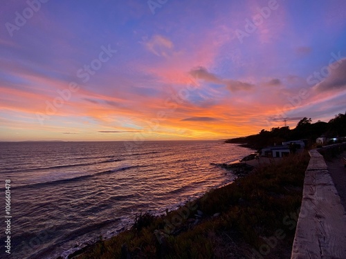 Atardecer en la costa de Tarifa, Andalucía, el cielo color añil y las nubes anaranjadas por los últimos rayos del sol, cae la noche y las aguas calmas de la baja marea, visto desde el sendero de fondo