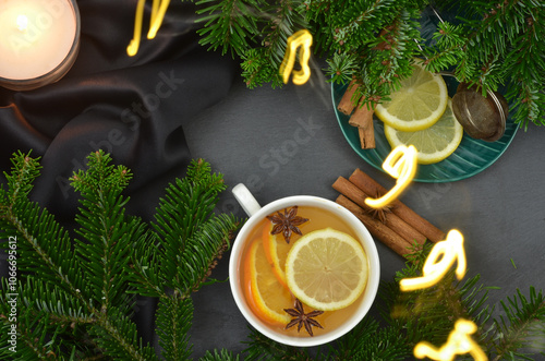 Christmas lights in the evening - Christmas tree branches and a cup of tea with lemon, orange and anise stars, cinnamon sticks, candle. Top view.