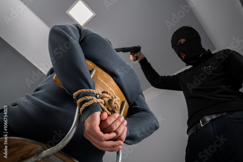 Masked man, thief, kidnapper holding gun to kidnapped person's head, criminal concept