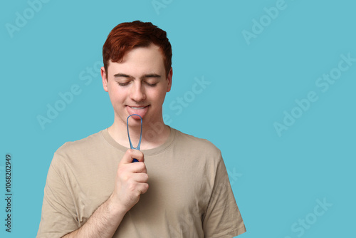 Young man with tongue scraper on blue background