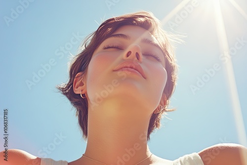 Woman Enjoying Sunlight with Closed Eyes, Close-up of a young woman with eyes closed, basking in sunlight against a clear blue sky, capturing a serene and peaceful moment.