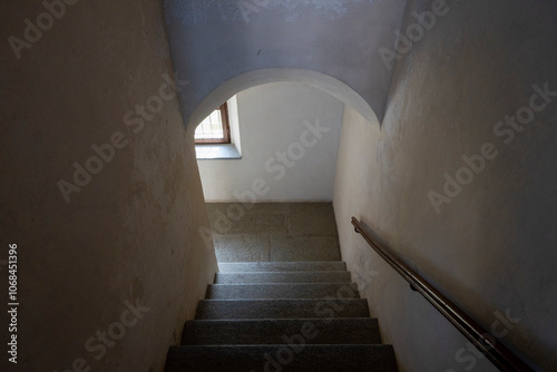 Interno, scala antica che scende verso finestra da cui proviene la luce.