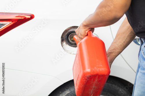 young man holds red gallon of gasoline which is reserve gasoline for emergency use when running out of fuel during trip or using reserve gasoline in red gallon to help people who run out of fuel.