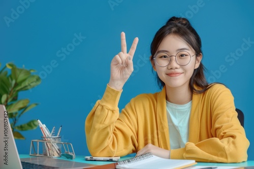 Asian student in glasses giving okay sign while studying online.