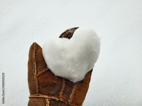 A heart made of snow lies on a brown tanned mitten. The concept of love, romance, Valentine's Day, Christmas