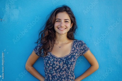 A woman stands in front of a blue wall, looking straight ahead