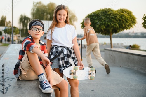 Cute kids in stylish casual clothes in skate park. They ride on skates and scooters. Summer vacation