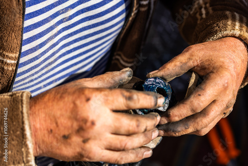 Dirty and calloused hands of a mechanic assembling compressed coil spring during DIY car repairs. Closeup.