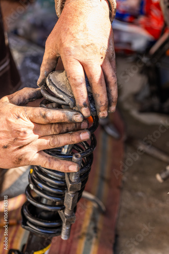 Dirty and calloused hands of a mechanic assembling compressed coil spring during DIY car repairs. Closeup.