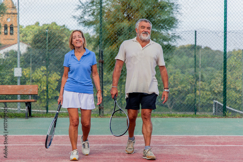 Senior tennis couple walking toward camera preparing for match in the club