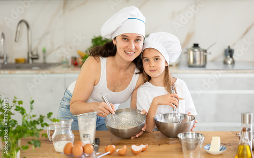 Happy mother and her daughter whisking ingredients in a bowl using metal corolla in the kitchen