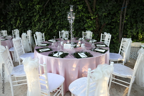 An elegant outdoor wedding reception table setting with white linens, gold accents, and lush floral arrangements